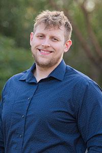 White man with light brown hair wearing a dark blue button up shirt